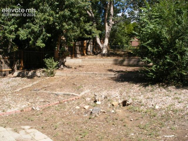 Image 32 of 35: Terraced backyard featuring mature trees, wooden fencing, and concrete reta
