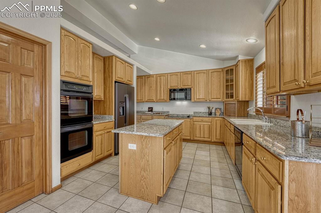 Image 12 of 50: Kitchen featuring light stone countertops, black appliances, vaulted ceilin