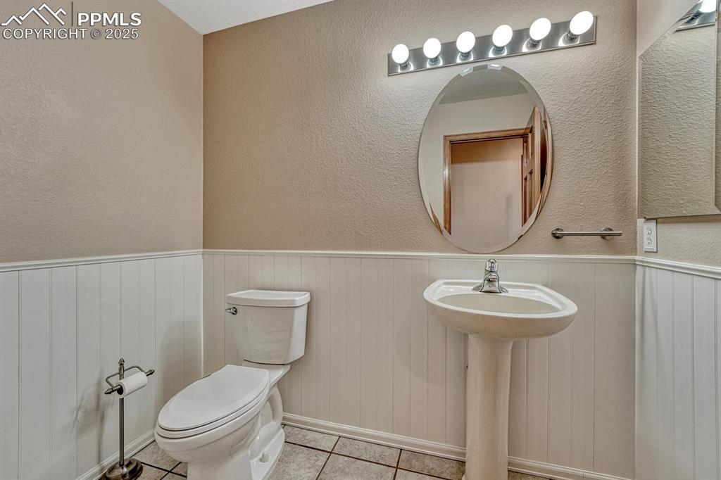 Image 23 of 50: Bathroom with a textured wall, tile patterned flooring, and wainscoting