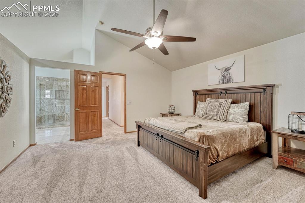 Image 24 of 50: Bedroom featuring vaulted ceiling, light carpet, a ceiling fan, and ensuite