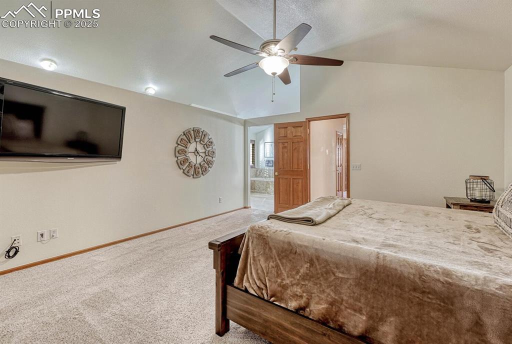 Image 25 of 50: Bedroom with vaulted ceiling, carpet, a ceiling fan, and ensuite bath