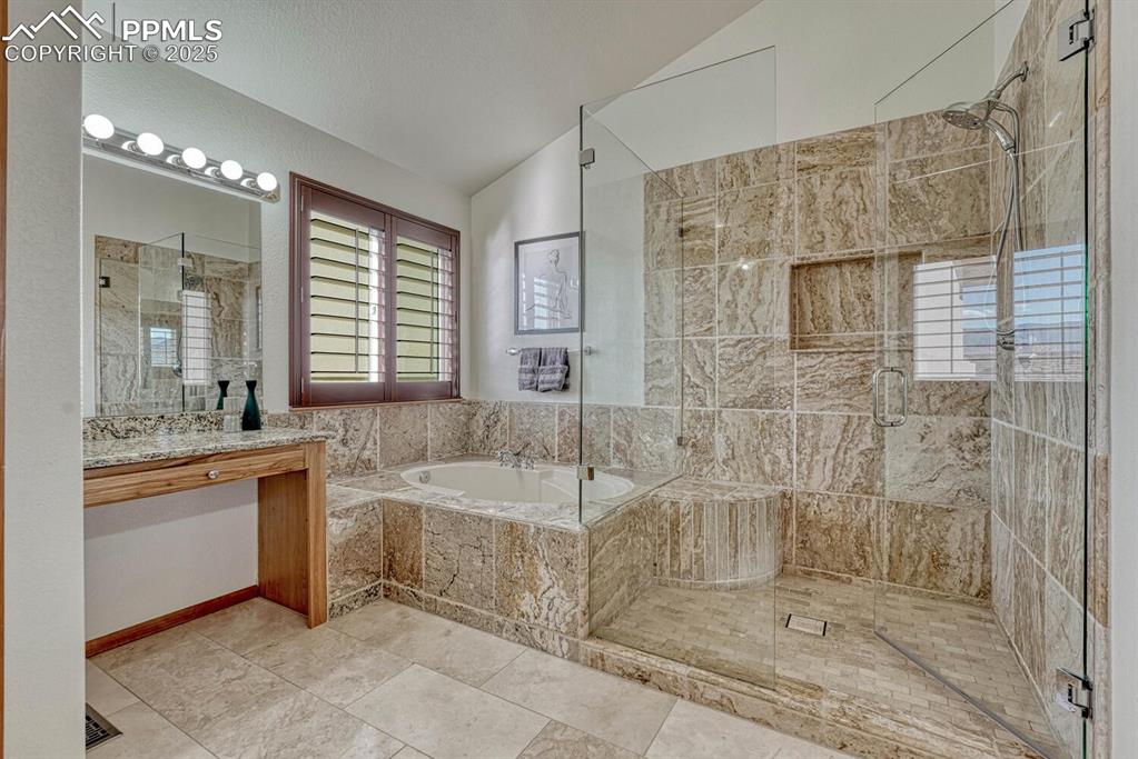 Image 28 of 50: Bathroom with lofted ceiling, a garden tub, a shower stall, vanity, and lig