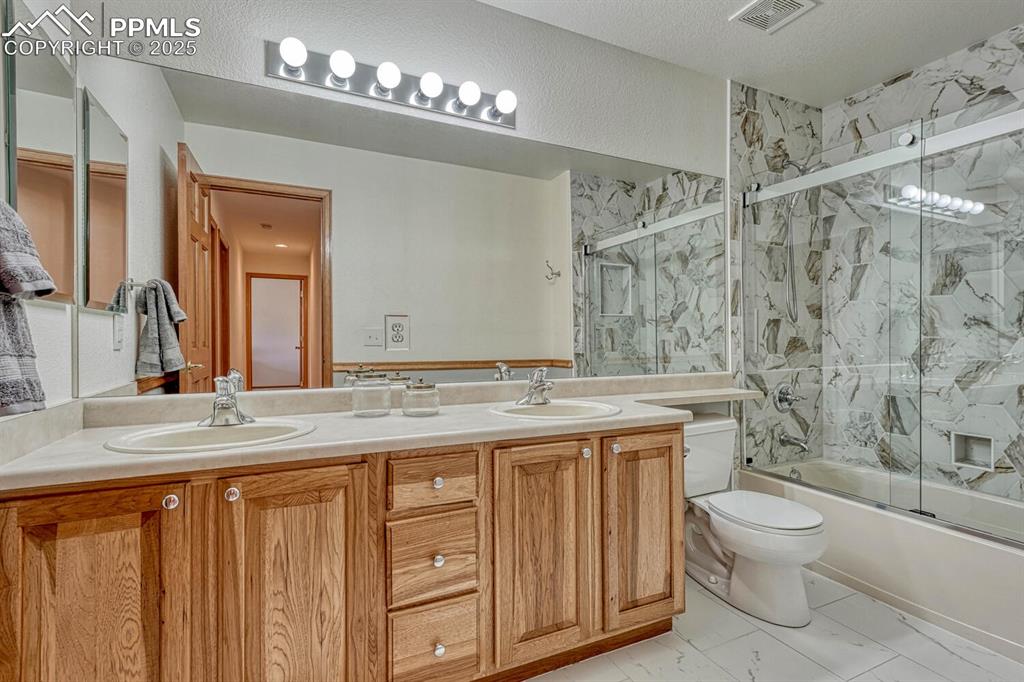 Image 30 of 50: Bathroom with double vanity and shower / bath combination with glass door