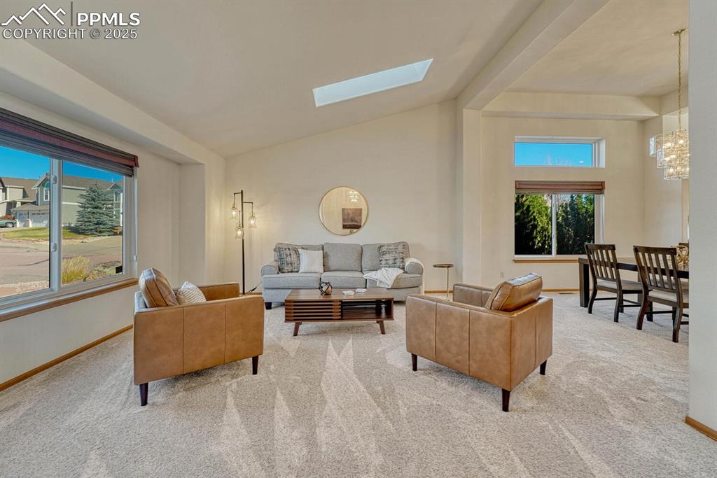 Image 5 of 50: Carpeted living area with a skylight, high vaulted ceiling, and a chandelie