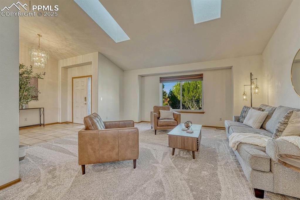 Image 6 of 50: Carpeted living area featuring lofted ceiling, a chandelier, a skylight, an