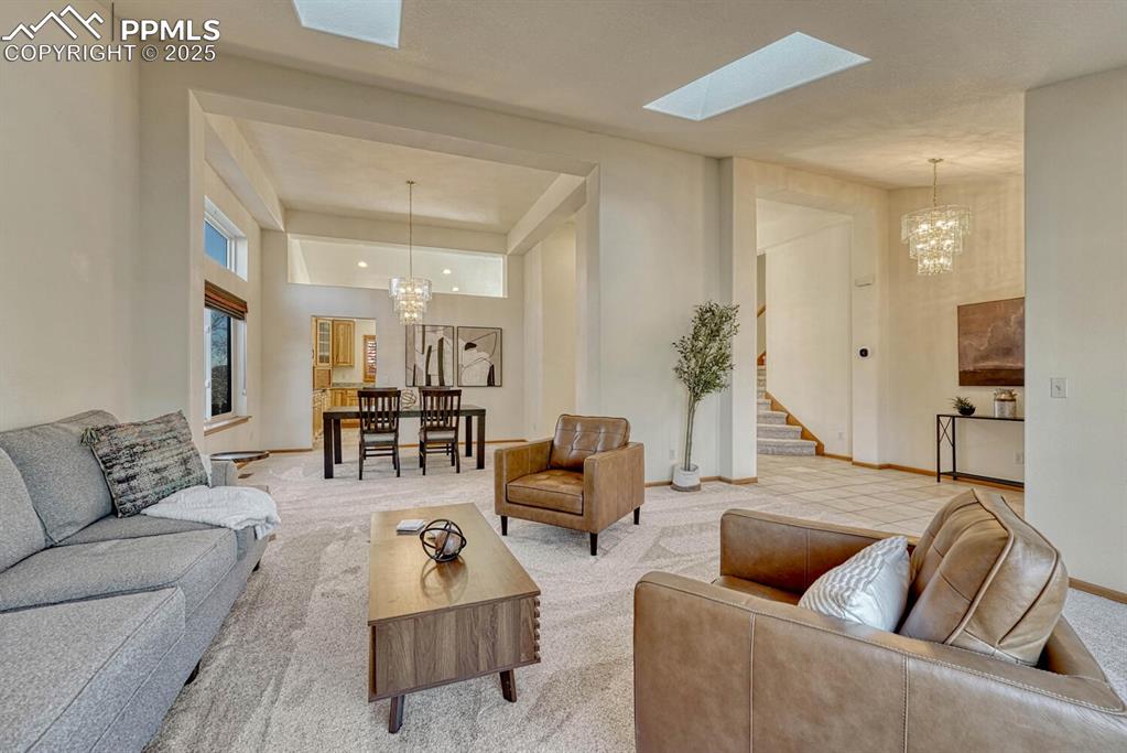 Image 7 of 50: Living area with a chandelier, carpet flooring, a skylight, and stairs