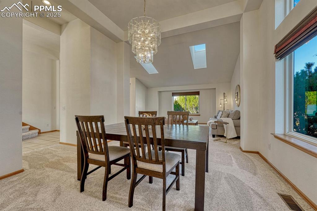 Image 8 of 50: Dining space with a towering ceiling, light colored carpet, a skylight, a c