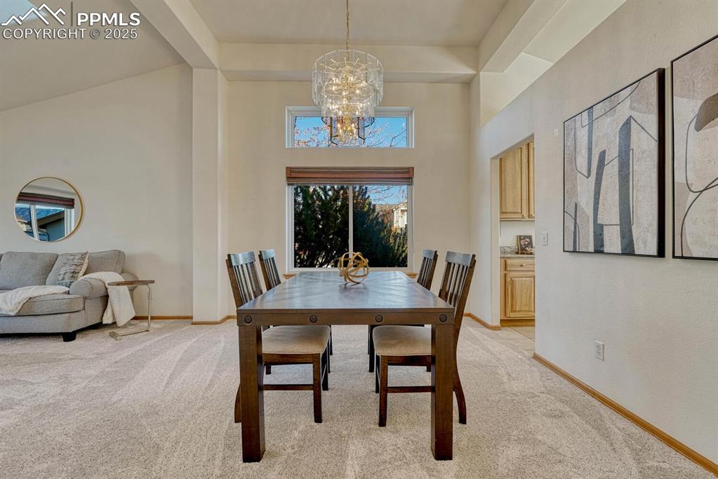Image 9 of 50: Dining space with light colored carpet, beam ceiling, a high ceiling, and a