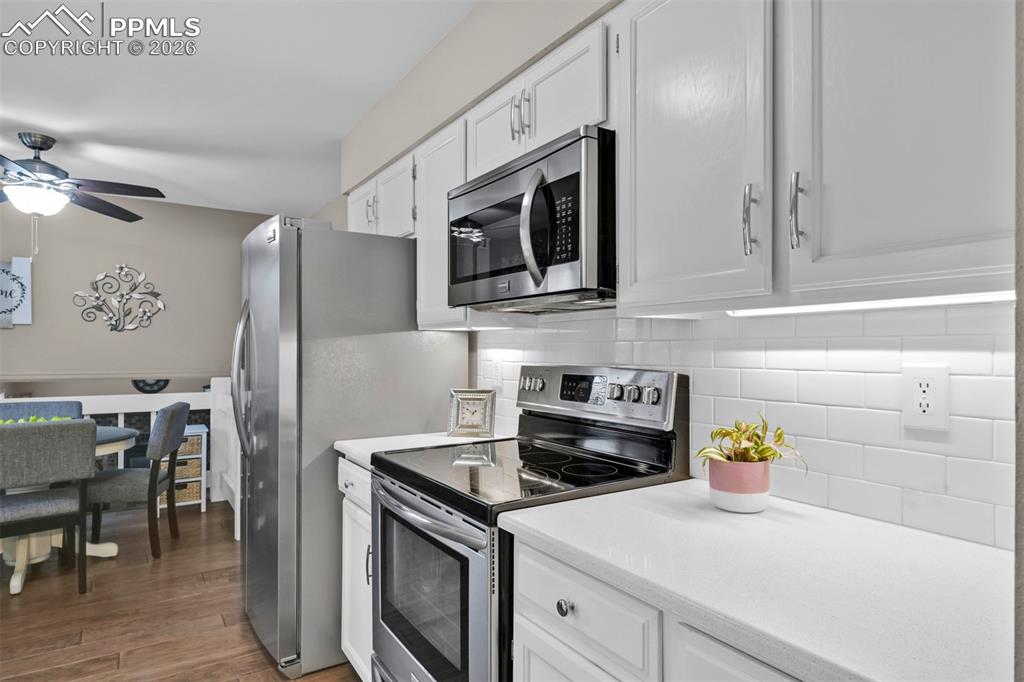Image 21 of 41: Kitchen featuring stainless steel appliances, white cabinetry, dark wood fi
