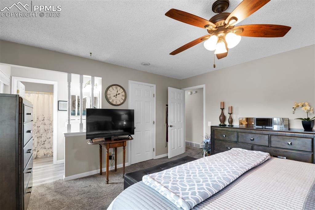 Image 30 of 41: Carpeted bedroom with a textured ceiling, a ceiling fan, and ensuite bathro