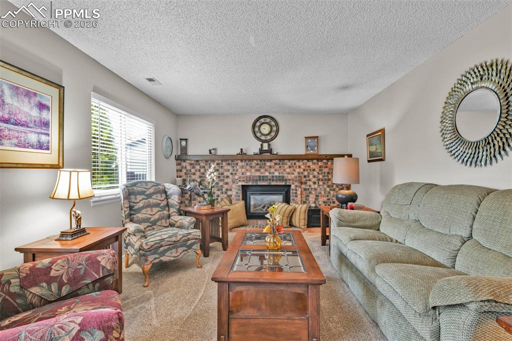 Image 37 of 41: Carpeted living area featuring a brick fireplace and a textured ceiling