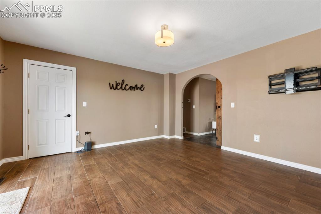 Image 11 of 39: Empty room with arched walkways, wood finished floors, and baseboards