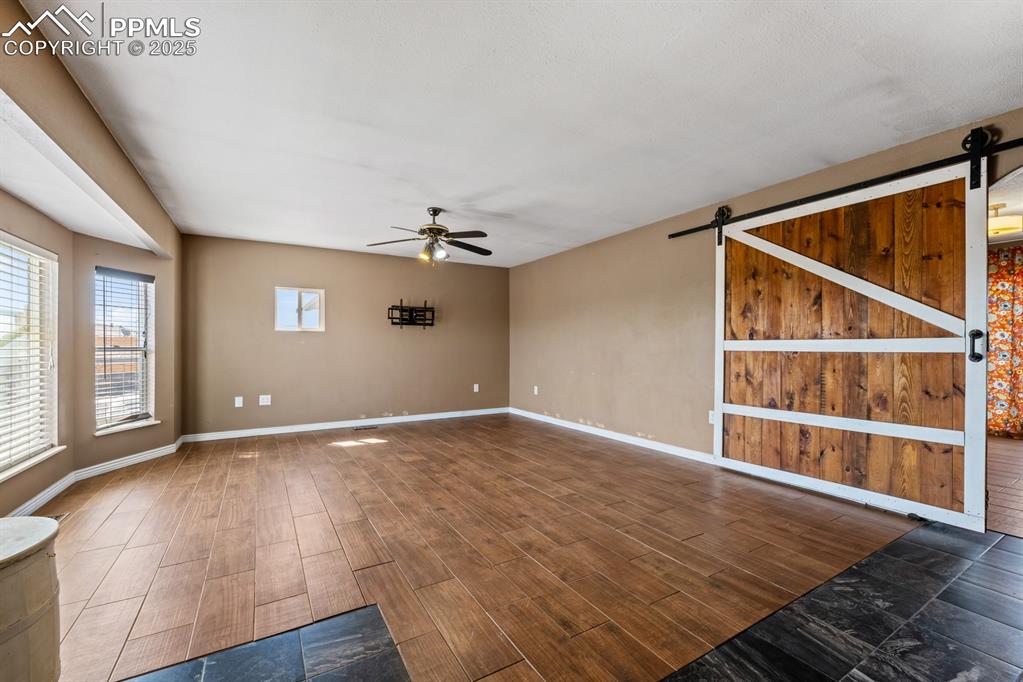 Image 6 of 39: Spare room featuring a barn door, ceiling fan, wood finished floors, and ba