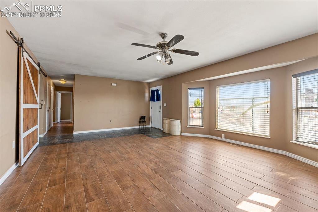 Image 7 of 39: Unfurnished living room with a barn door, a ceiling fan, wood finished floo