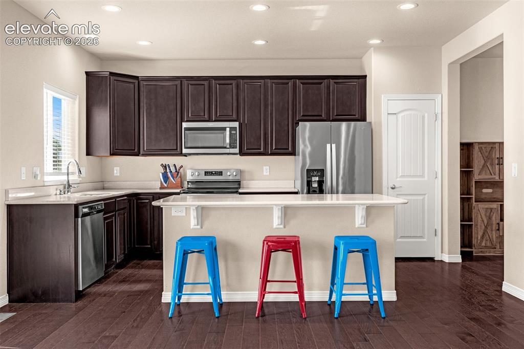 Image 10 of 45: Kitchen featuring dark wood-finish cabinetry, light countertops, stainless