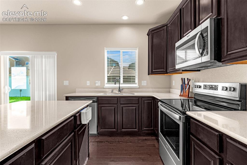 Image 13 of 45: Rich wood-finish cabinetry, light-toned countertops, and stainless steel ap