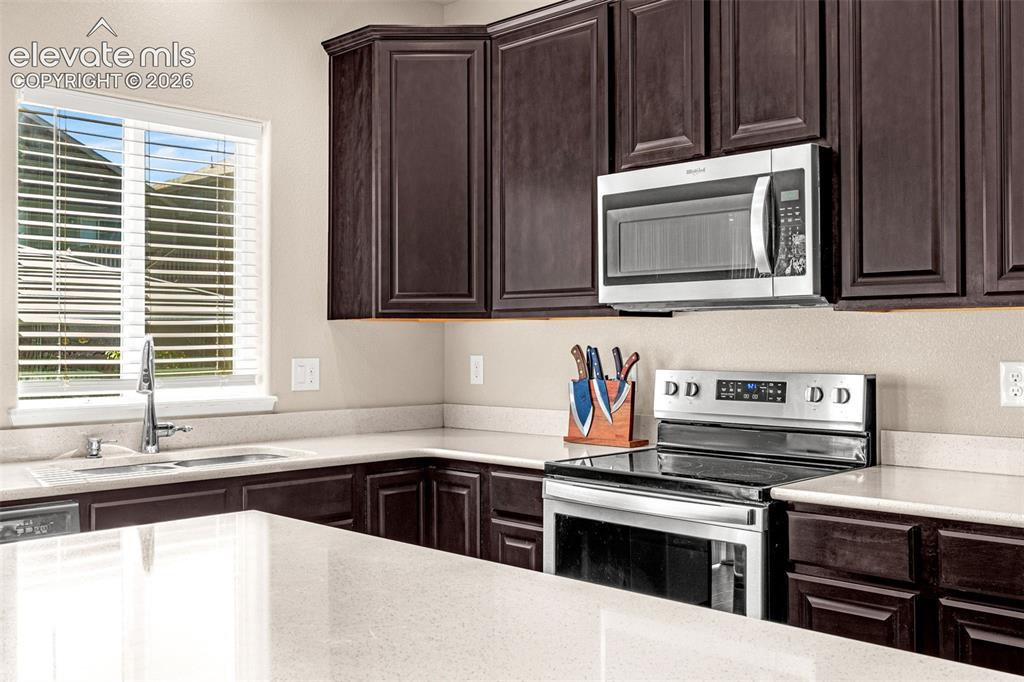 Image 15 of 45: Dark wood-finish cabinetry, light-toned countertops, stainless steel applia