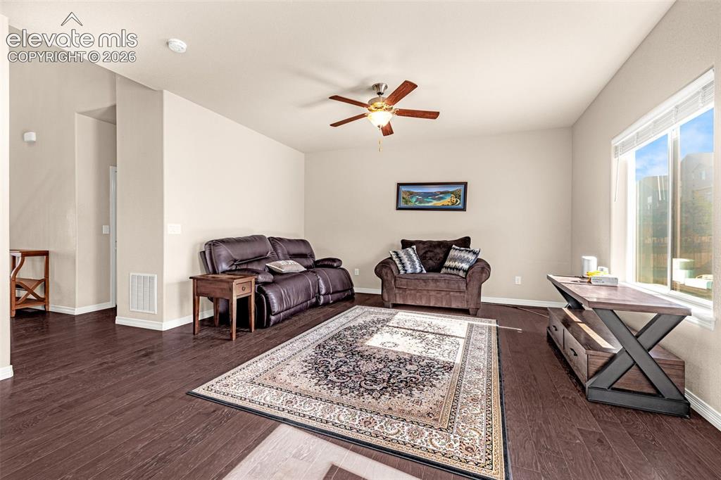 Image 8 of 45: Spacious living area featuring wood-finish flooring, a ceiling fan, and lar
