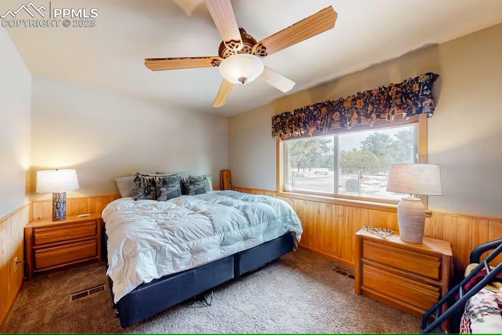 Image 16 of 36: Bedroom 1 featuring wooden walls, visible vents, carpet flooring, and wains