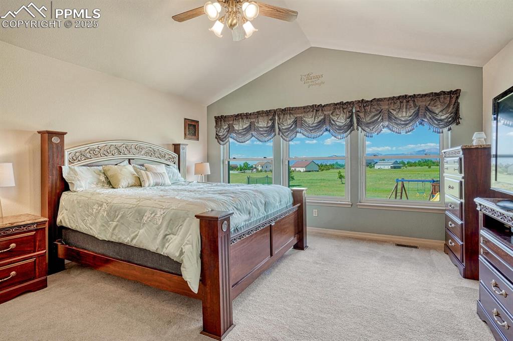 Image 25 of 50: Vaulted Main Level Primary Bedroom with neutral carpet, lighted ceiling fan