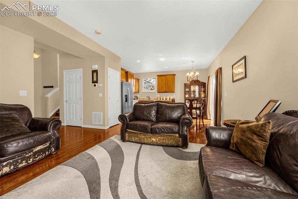 Image 4 of 23: Living area with wood finished floors, stairs, a chandelier, baseboards, an