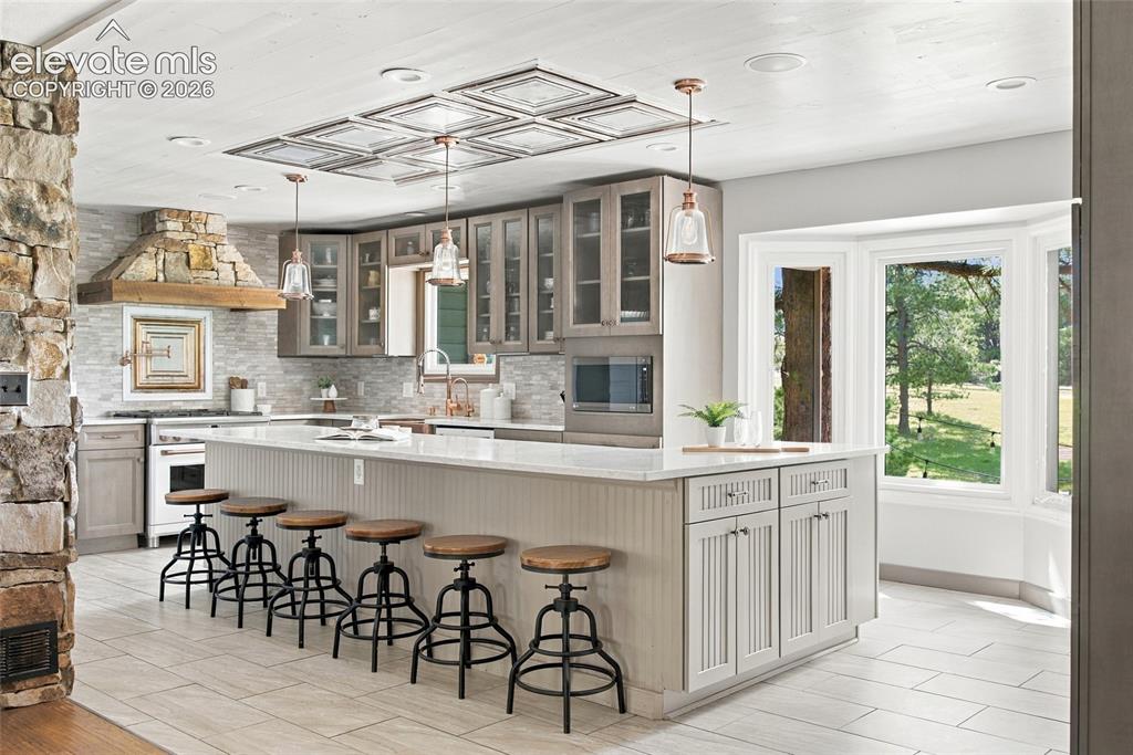Image 2 of 37: Kitchen featuring a stone-clad range hood, white tile backsplash, a large c