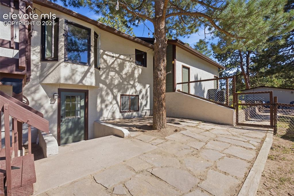 Image 27 of 37: Stucco exterior with a bay window, natural stone patio, concrete walkway, a