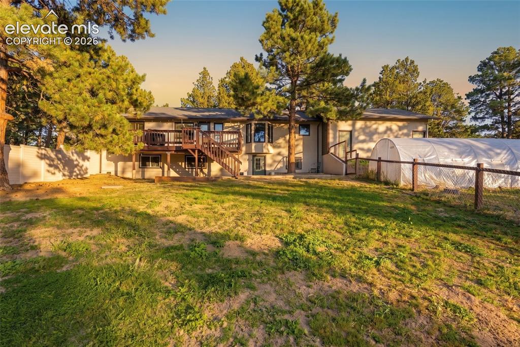 Image 28 of 37: Expansive grassy yard with mature trees, a wood deck with stairs, a partial