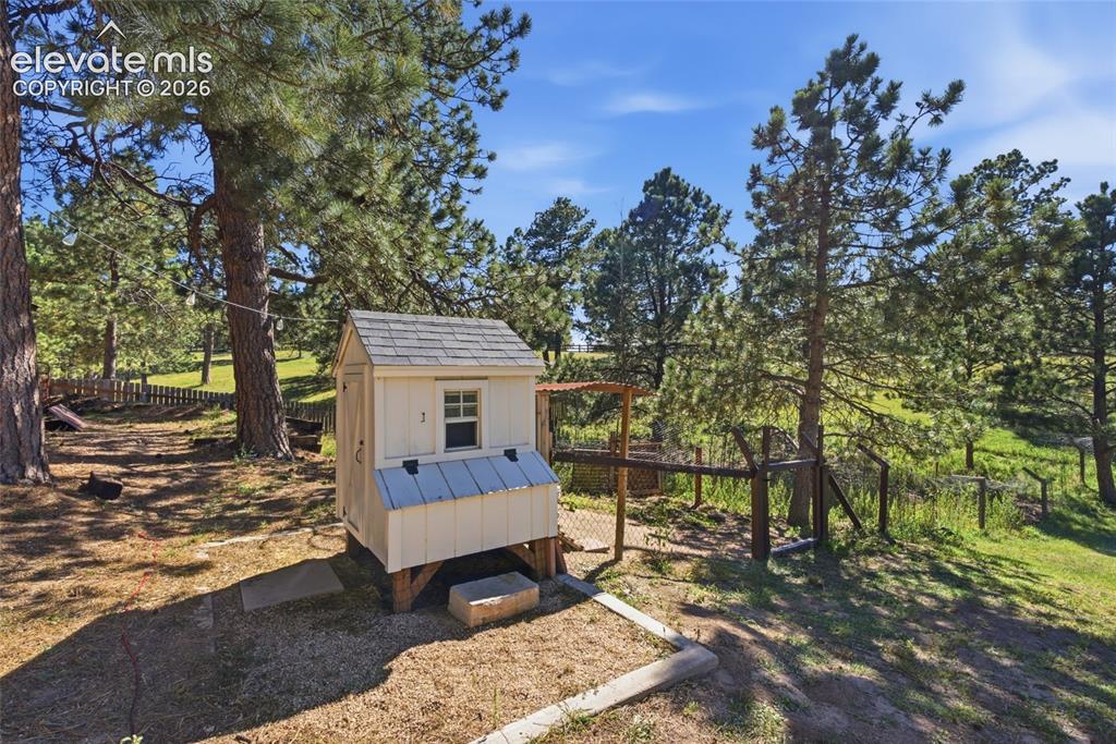 Image 32 of 37: Fenced enclosure with a chicken coop, surrounded by mature trees and natura