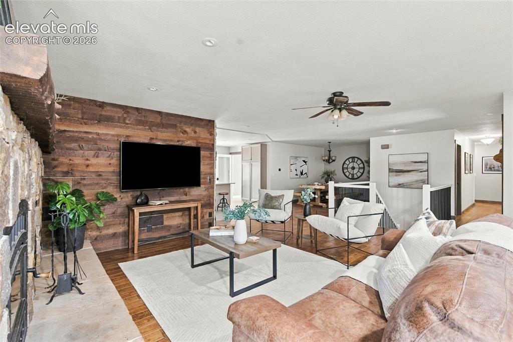 Image 7 of 37: Stone fireplace with a wood mantel, wood-finish flooring, and a wood-panele