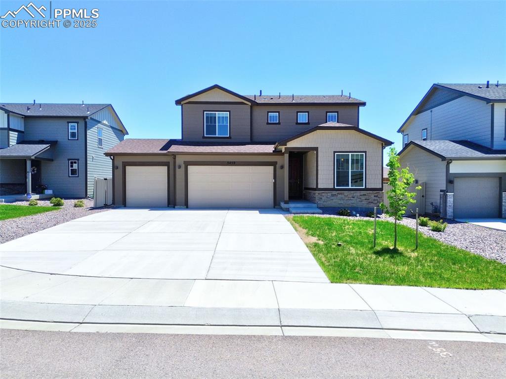 Caption: View of front facade with driveway, an attached garage, a front lawn, and stone siding