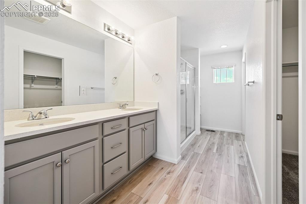 Image 21 of 24: Bathroom with a walk in closet, double vanity, and a stall shower