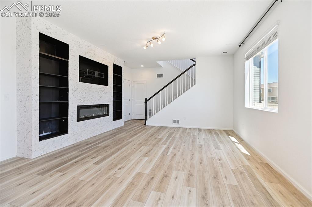 Image 8 of 24: Unfurnished living room featuring built in features, a large fireplace, sta