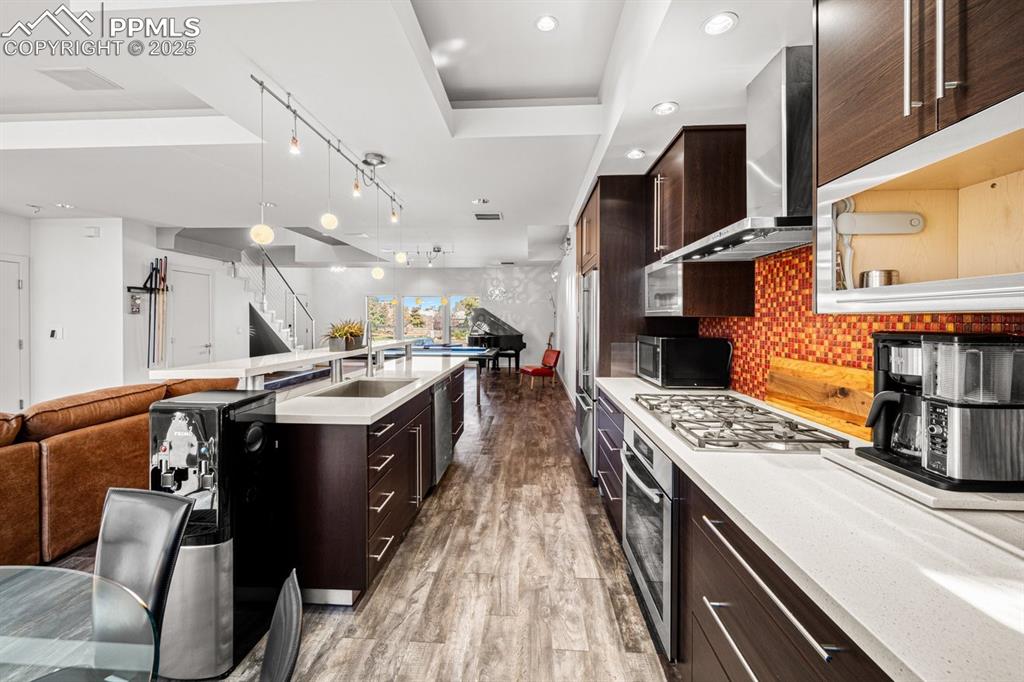 Image 10 of 41: Kitchen with dark brown cabinetry, open floor plan, tasteful backsplash, da