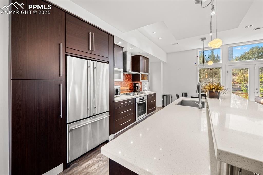 Image 6 of 41: Kitchen with dark brown cabinetry, stainless steel appliances, light stone 