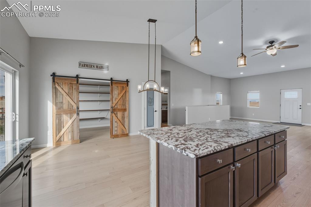 Image 11 of 50: Kitchen featuring light stone counters, a barn door, hanging light fixtures