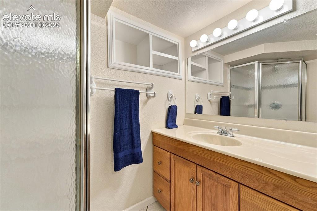 Image 35 of 48: Shower with textured glass enclosure, wood-finish vanity with integrated si