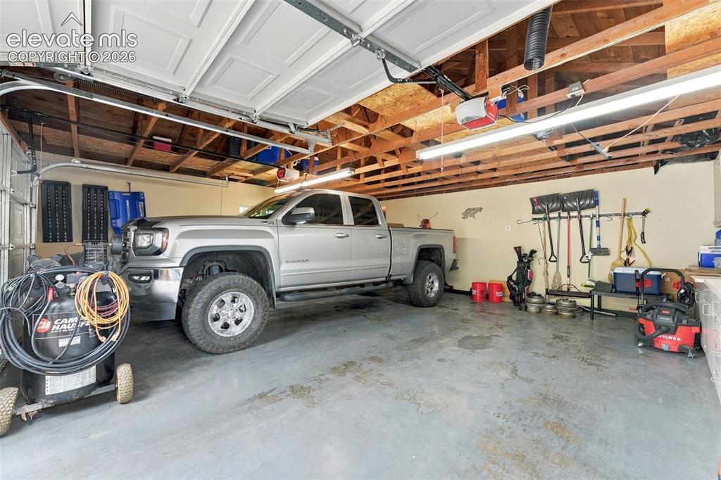 Image 40 of 48: Attached garage with concrete flooring, exposed wood beam ceiling, and fluo