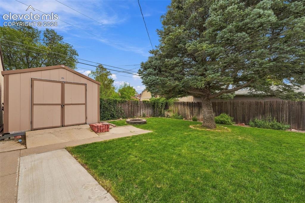 Image 41 of 48: Expansive green lawn, mature shade tree, concrete patio, fire pit, and a st