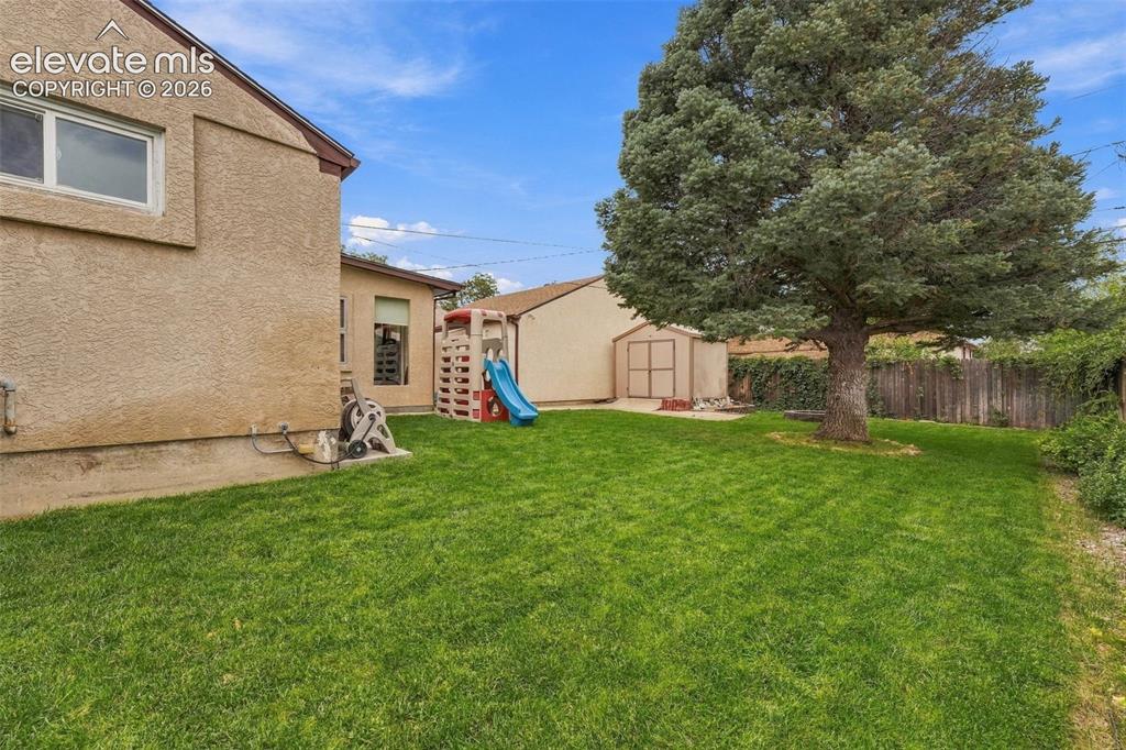 Image 43 of 48: Expansive backyard with a manicured lawn, mature tree, and wood-paneled pri