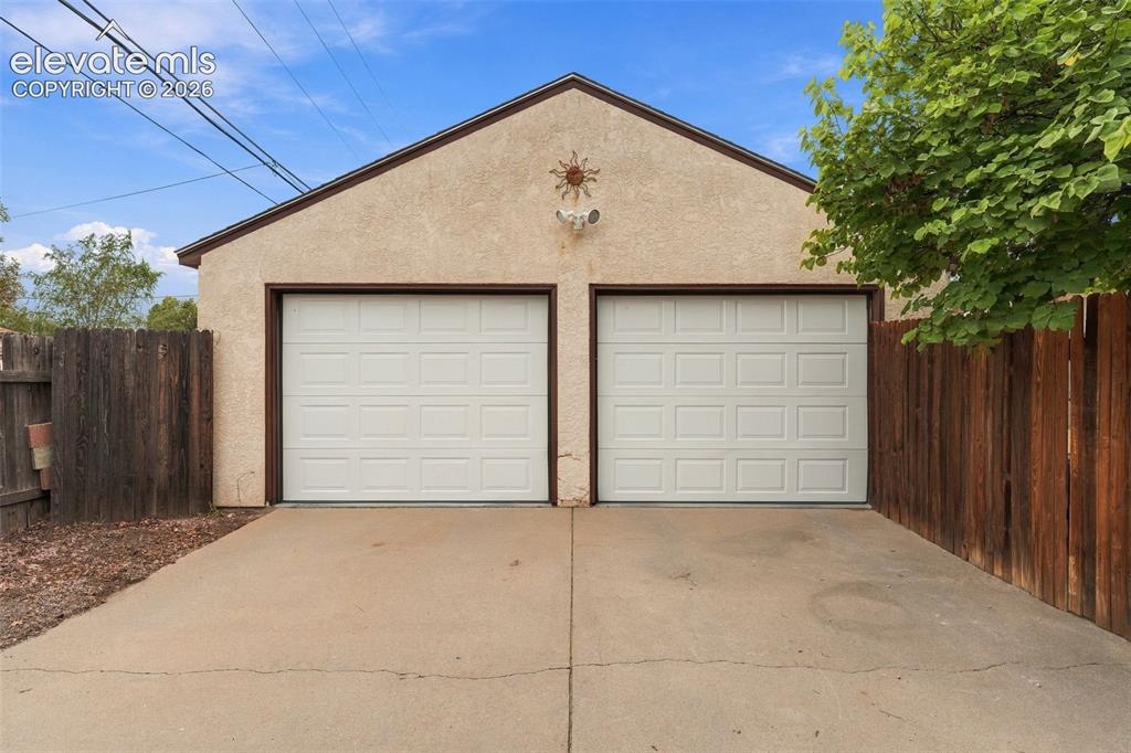 Image 47 of 48: Two white panel garage doors with stucco exterior, concrete driveway, and w