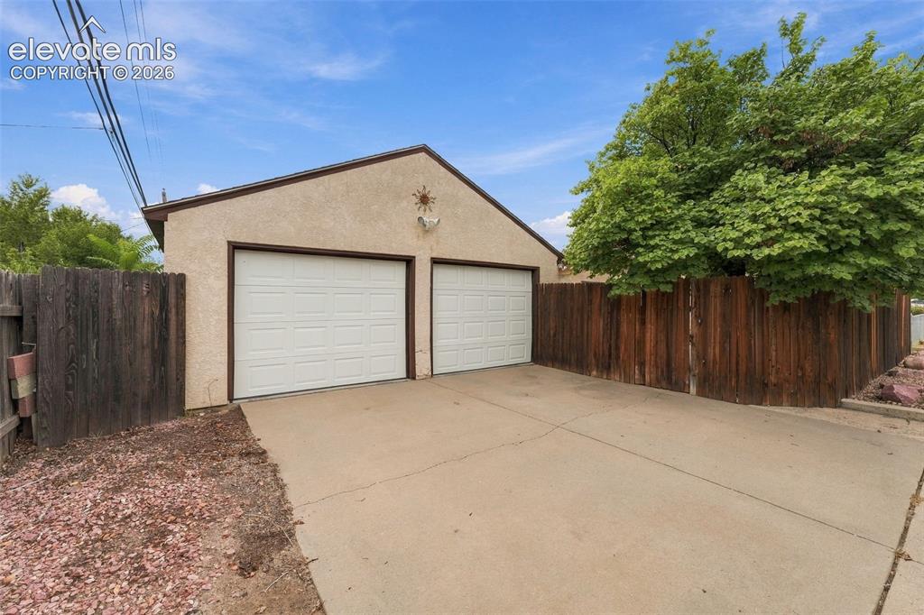 Image 48 of 48: Two-car garage with individual white panel doors, stucco exterior, and a co
