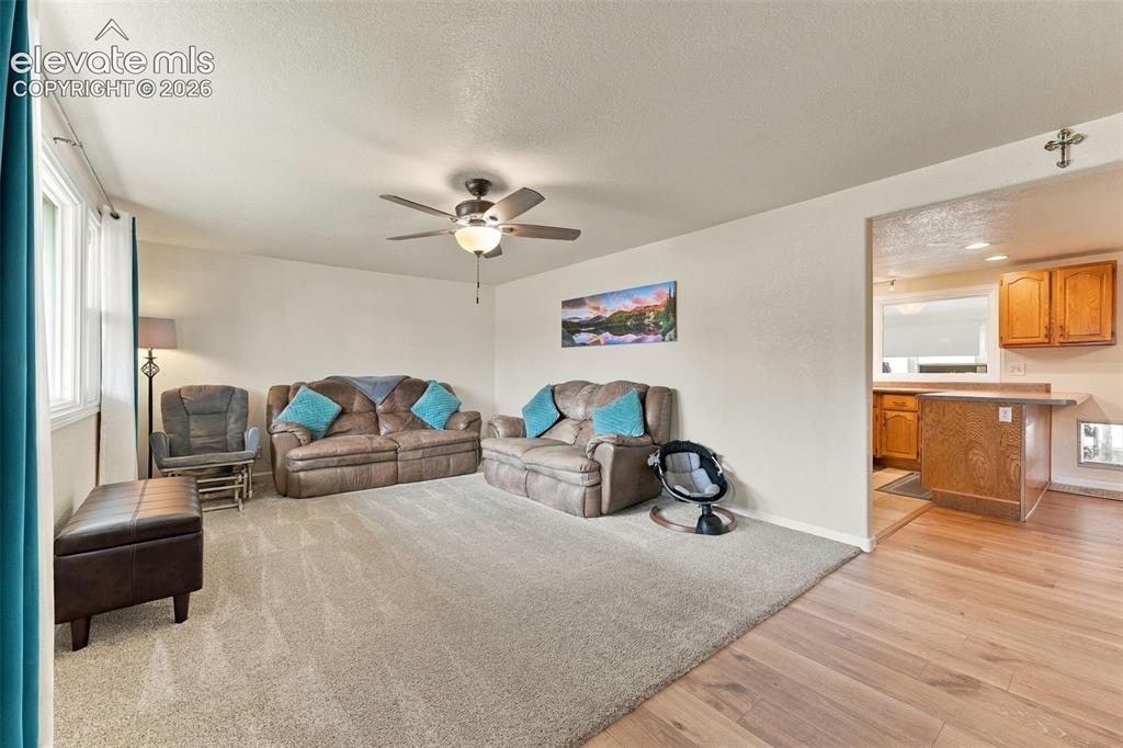 Image 6 of 48: Carpeted living area with a ceiling fan light fixture, large window, and wo