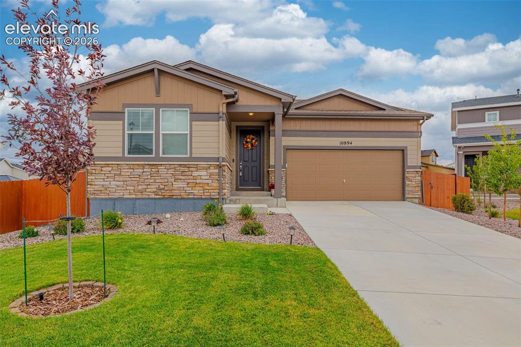 Caption: Single-story exterior with stone and siding accents, attached garage, concrete driveway, and a lands