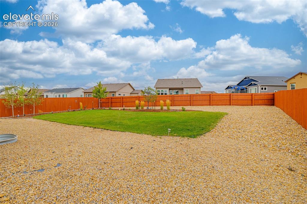 Image 31 of 40: Expansive backyard featuring a manicured lawn, gravel landscaping, and wood
