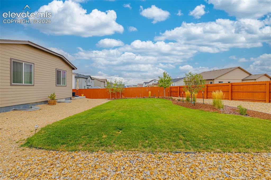 Image 32 of 40: Expansive backyard featuring a manicured lawn, gravel perimeter, mature tre