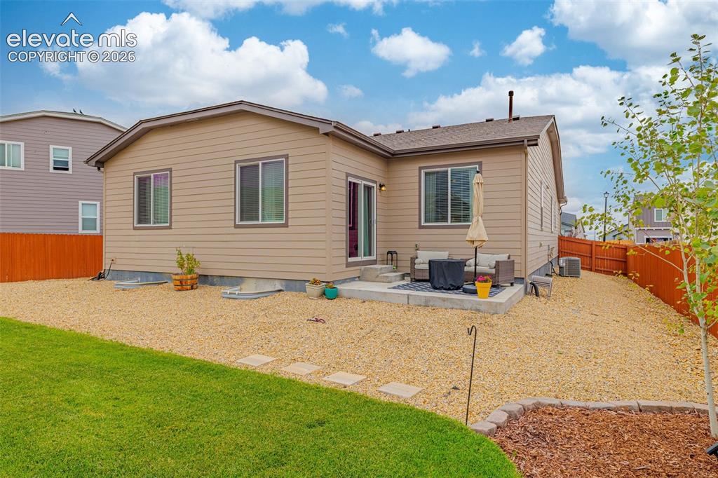 Image 33 of 40: Tan siding exterior with a concrete patio, sliding glass door, and a brown 