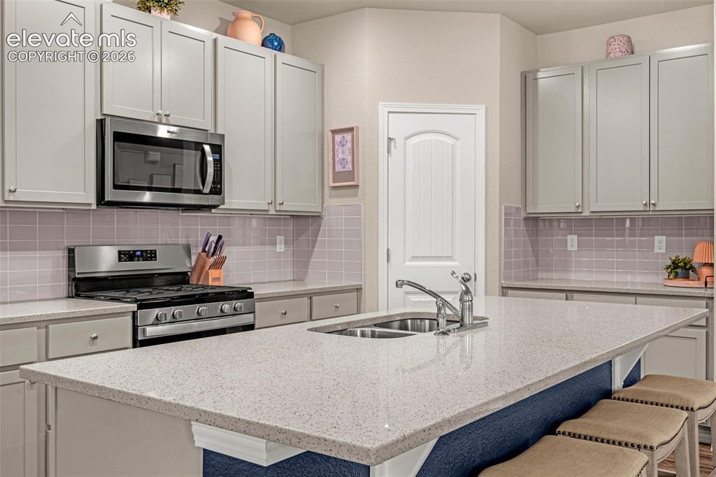 Image 4 of 40: Kitchen featuring an island with a double basin sink, light-toned counterto