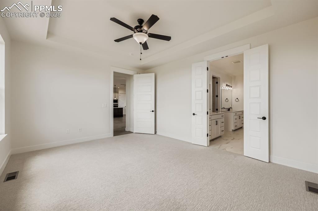 Image 15 of 29: Unfurnished bedroom with a tray ceiling, light colored carpet, and connecte