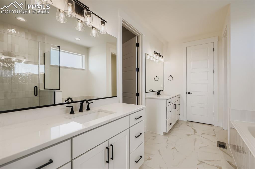 Image 16 of 29: Bathroom featuring two vanities, a shower stall, a garden tub, marble look 